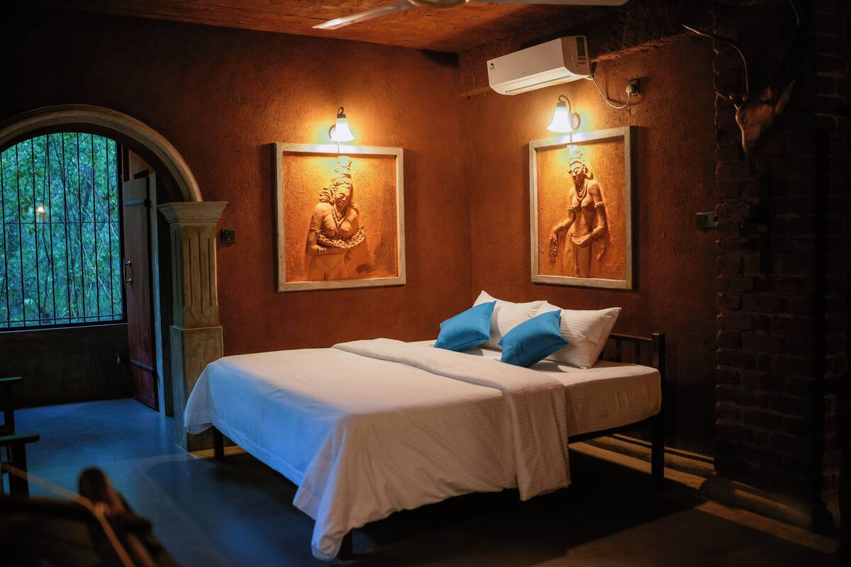Een slaapkamer met een groot bed, twee wandlampen, een raam met tralies en een bakstenen muur.