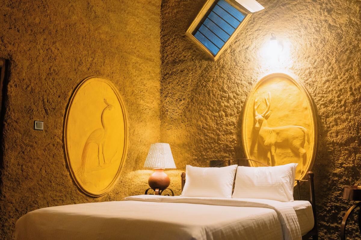 Een kamer met een bed, een lamp en twee ovale wandsculpturen van herten.