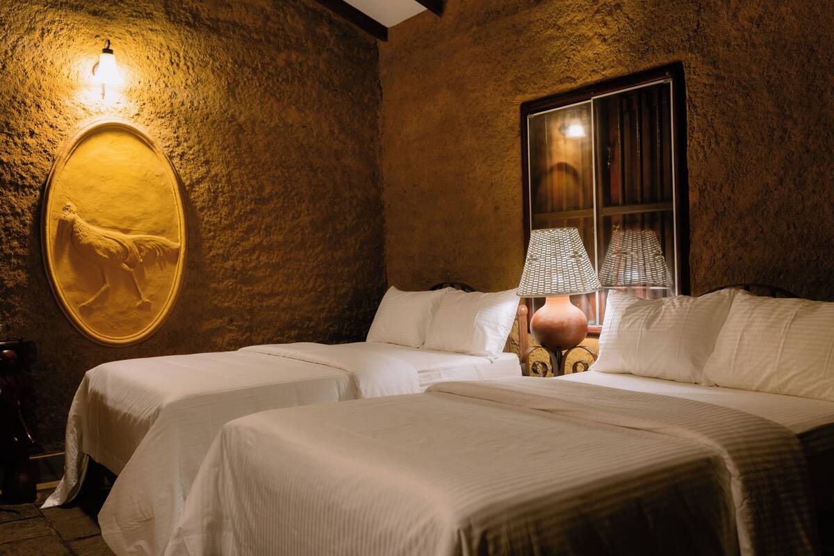 Een kamer met twee bedden, een lampje aan de muur en een raam met lamp.