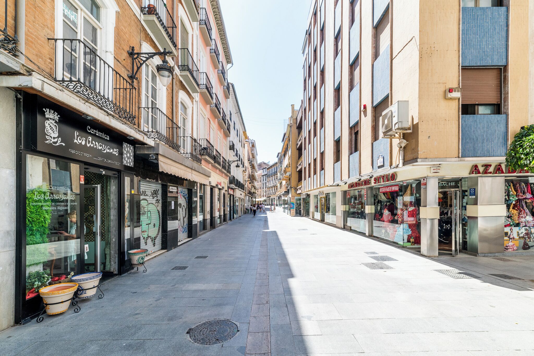 Calle con comercios a ambos lados, incluyendo una tienda de cerámica y una boutique.
