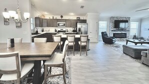 A modern kitchen with dark cabinets, a central island, and a dining area with a wooden table and chairs. - Into The Mystic - 3/2 Dog Friendly w/ Golf Cart in The Villages (St Catherine, The Villages)