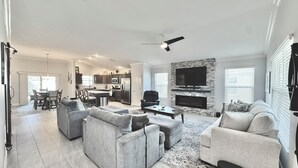 A spacious living room with grey sofas, a coffee table, and a fireplace. There is a kitchen in the background with modern appliances. - Into The Mystic - 3/2 Dog Friendly w/ Golf Cart in The Villages (St Catherine, The Villages)