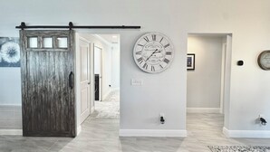A hallway with a rustic wooden door, a wall clock, and a framed picture. - Into The Mystic - 3/2 Dog Friendly w/ Golf Cart in The Villages (St Catherine, The Villages)
