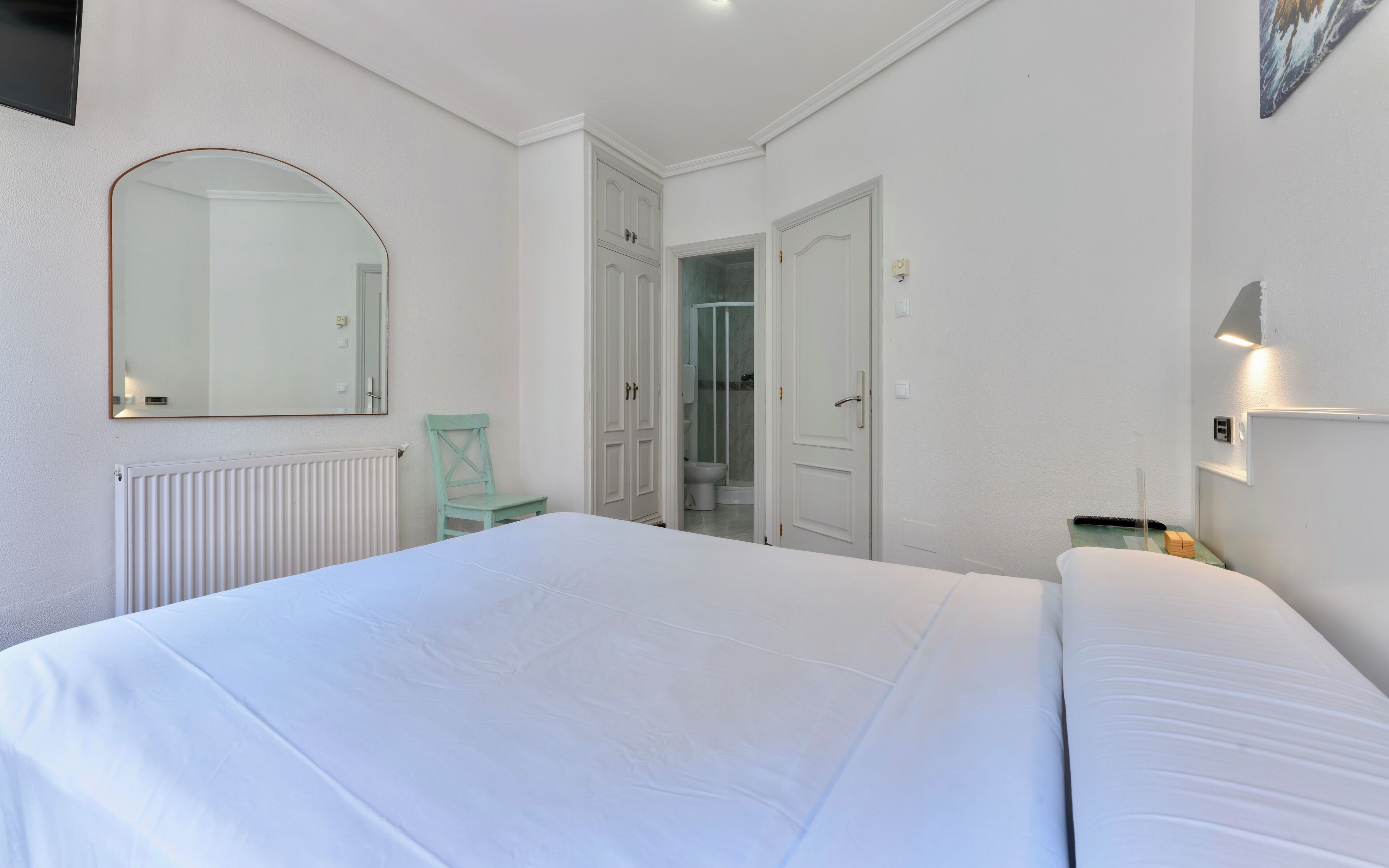 Un dormitorio con cama, una silla, una puerta, un espejo y un radiador.