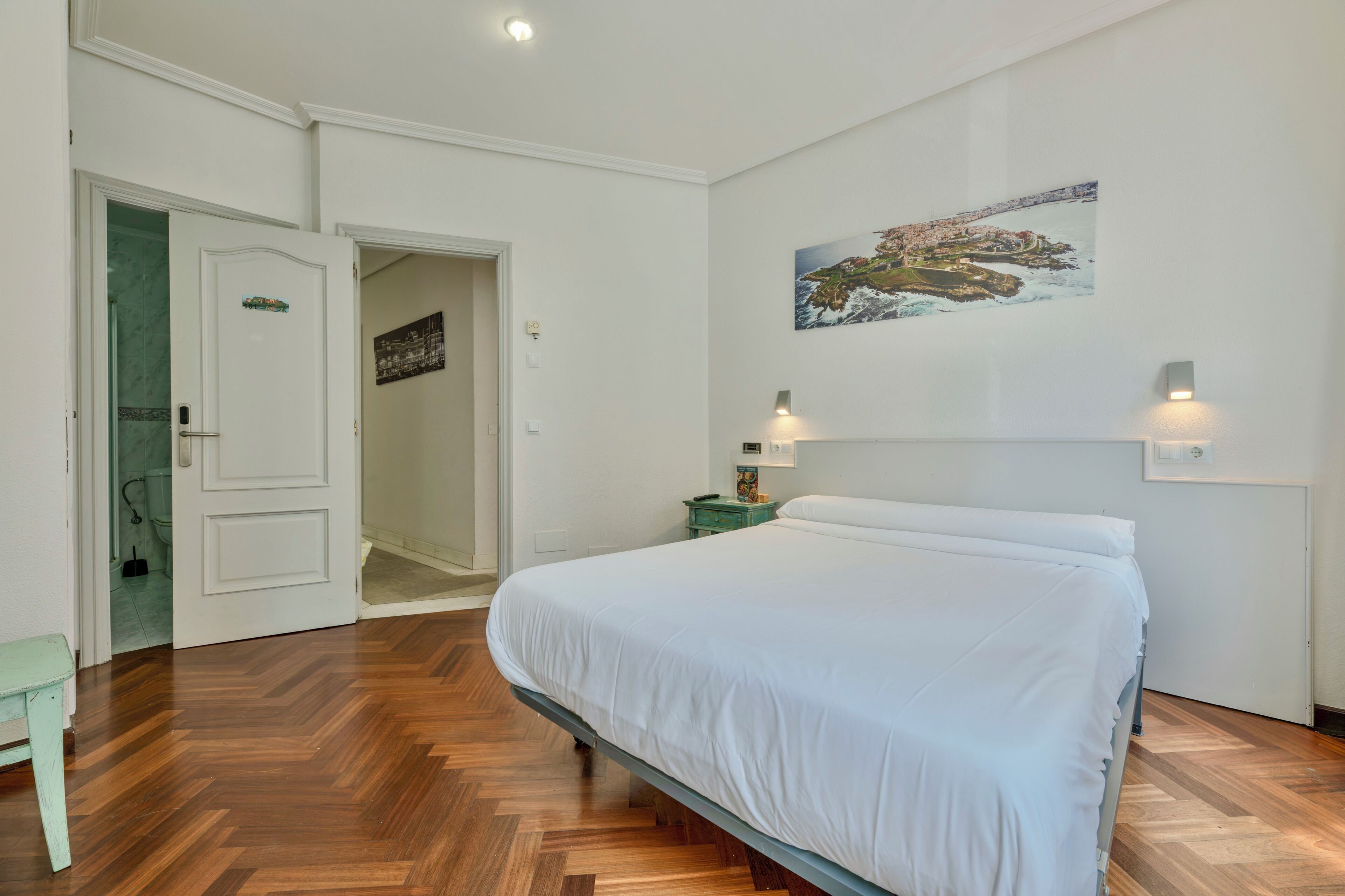 Un dormitorio con cama, mesita de noche, un cuadro y una puerta que da a un baño.