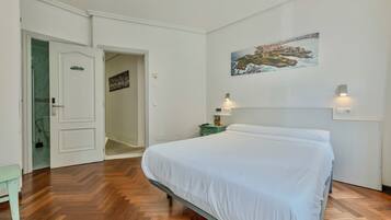 Un dormitorio con cama, mesita de noche, un cuadro y una puerta que da a un baño.
