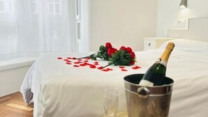 Une chambre d’hôtel avec un lit, une table de chevet sur laquelle se trouve une bouteille de champagne, un verre et une assiette de fraises.