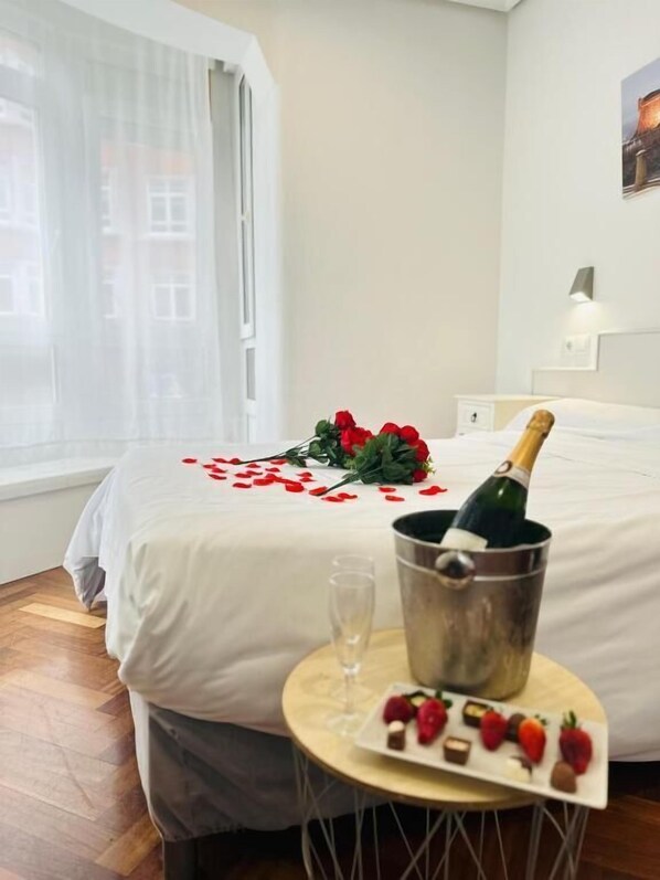 A hotel room with a bed, a bedside table with a bottle of champagne, a glass, and a plate of strawberries.