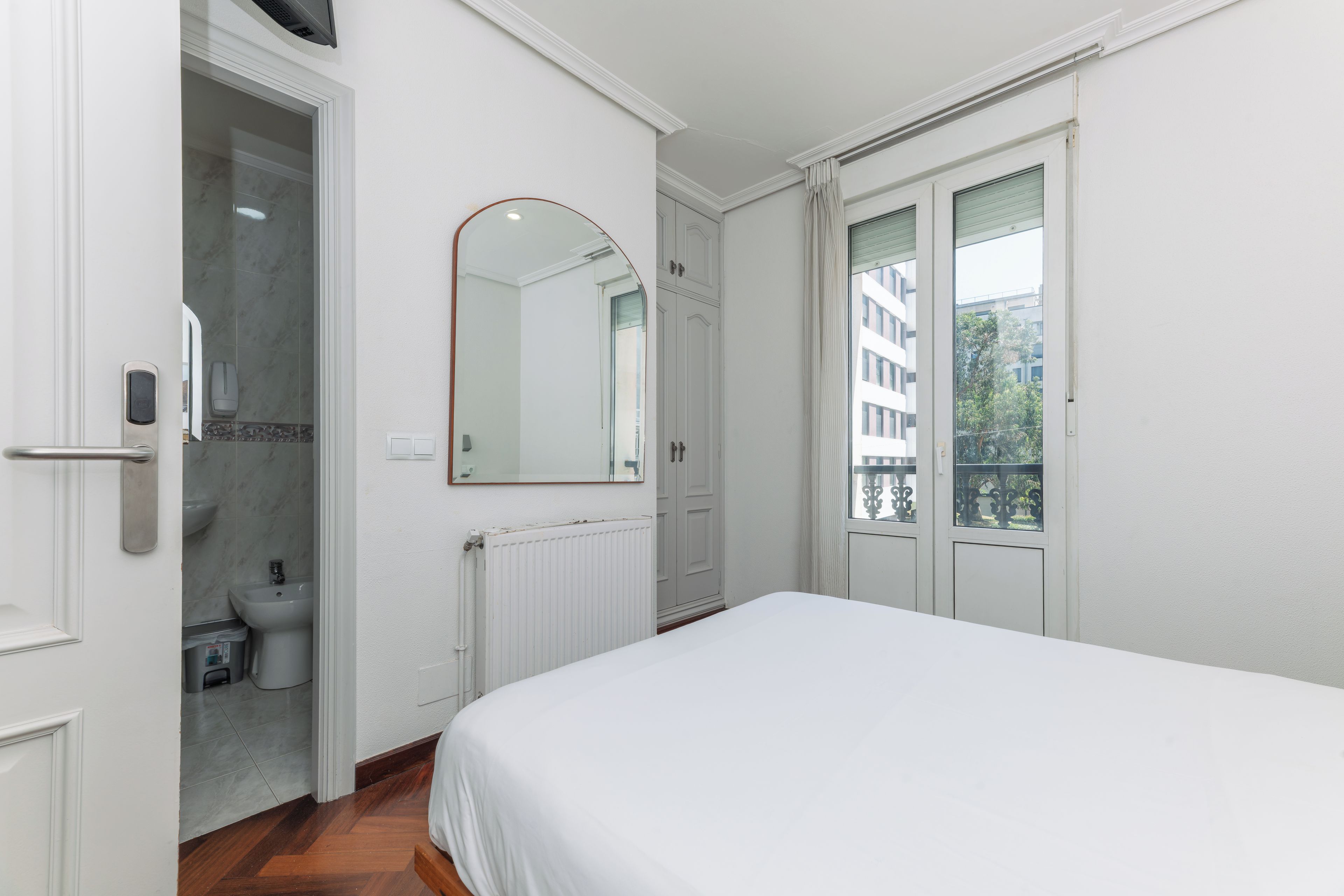 Une chambre avec un lit, une salle de bain avec des toilettes et une vue sur les bâtiments environnants.