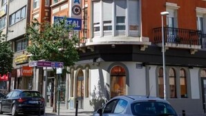 Un immeuble à plusieurs étages, sur lequel on peut voir un grand panneau indiquant « COSTA CORUNA », et qui présente un style architectural classique avec des coins arrondis et de nombreux balcons.