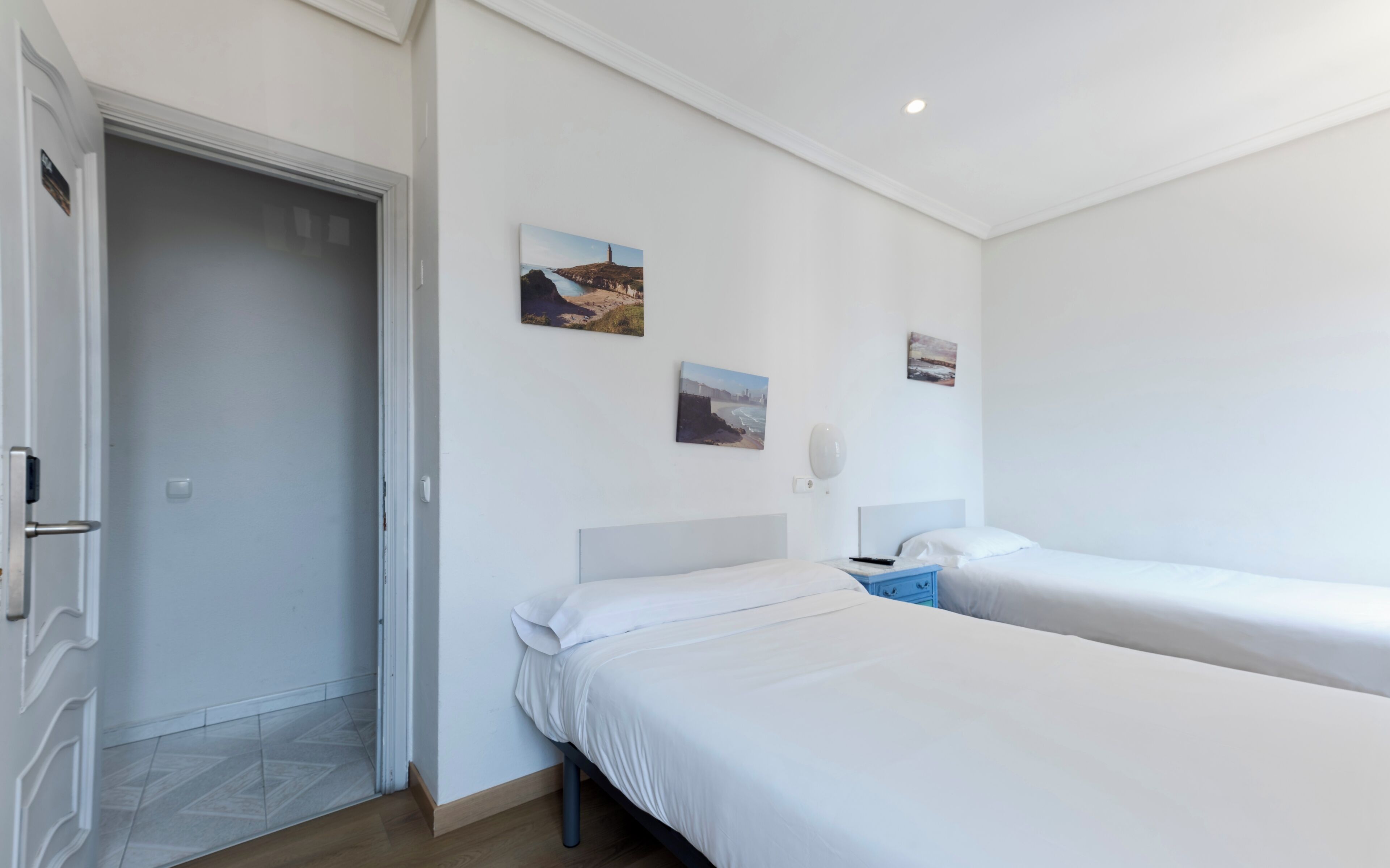 Een hotelkamer met twee bedden, een deur en kunstwerken aan de muur.
