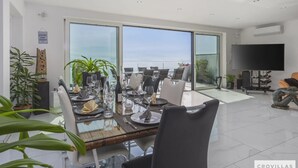 A dining area with a large table set for a meal, large windows offering a view of the sea, and a flat-screen TV on the wall. - Villa Diamond in Opatija - Crovillas (Opatija)