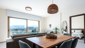 A modern living room with a wooden dining table, blue chairs, a large window with a view of mountains, and a hanging woven light fixture. - Elpida Luxury Villa, Private Pool, Fantastic View (Chania)