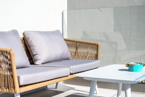 A wicker sofa with cushions, a white table, and a blue container on a balcony. - Elpida Luxury Villa, Private Pool, Fantastic View (Chania)