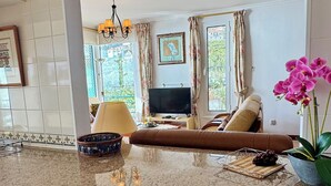 A kitchen with a granite countertop, a dining area with a brown leather sofa, and a view of a living room with a TV and curtains. - Apartamento Precioso | Large terrace, sea view and pool (Arco da Calheta)