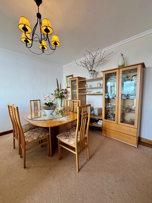 A dining room with a round glass table, wooden chairs, a chandelier, and a cabinet with glass doors. - Apartamento Precioso | Large terrace, sea view and pool (Arco da Calheta)