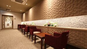 Een hotel receptie met een structuurwand, een receptiebalie en verschillende rode stoelen.
