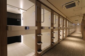 Reihenweise Stockbetten mit separaten Bedienelementen, ein Teppichboden und ein Korridor mit Deckenlüfter.