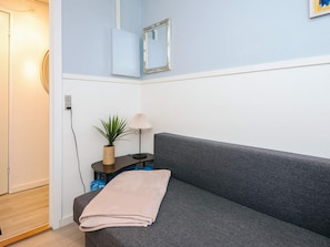 A room with a grey sofa, a small table with a lamp and a plant, a wall-mounted mirror, and a door. - 4 Star Holiday Home in Bording (Bording)