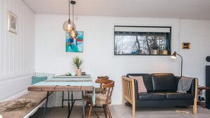 Ein gemütliches Wohnzimmer mit einer hölzernen Bank, einem schwarzen Ledersofa und einem Esstisch mit Stühlen.
