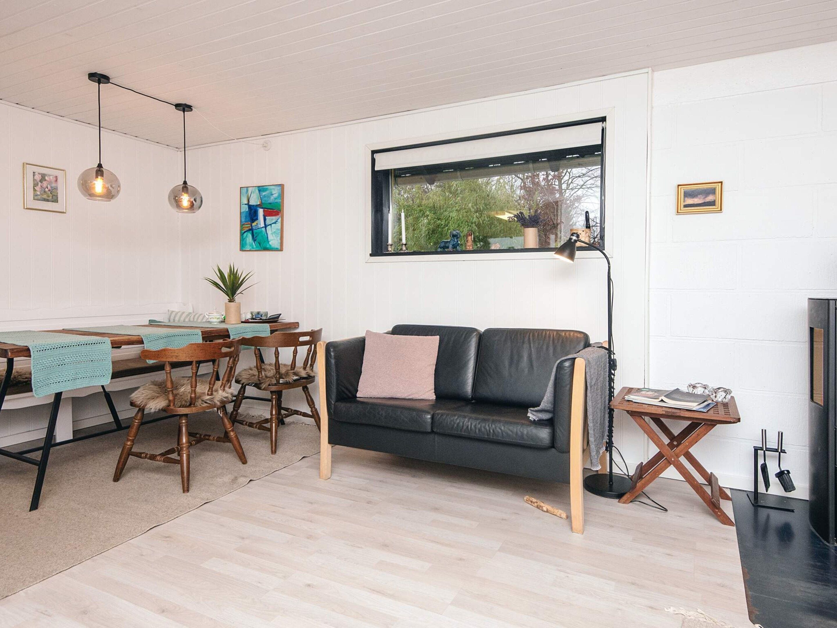 Un salon chaleureux avec un canapé en cuir noir, une table à manger en bois et des lampes suspendues.