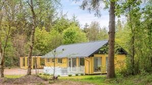 Ein gelbes Holzhäuschen mit Veranda, umgeben von Bäumen.