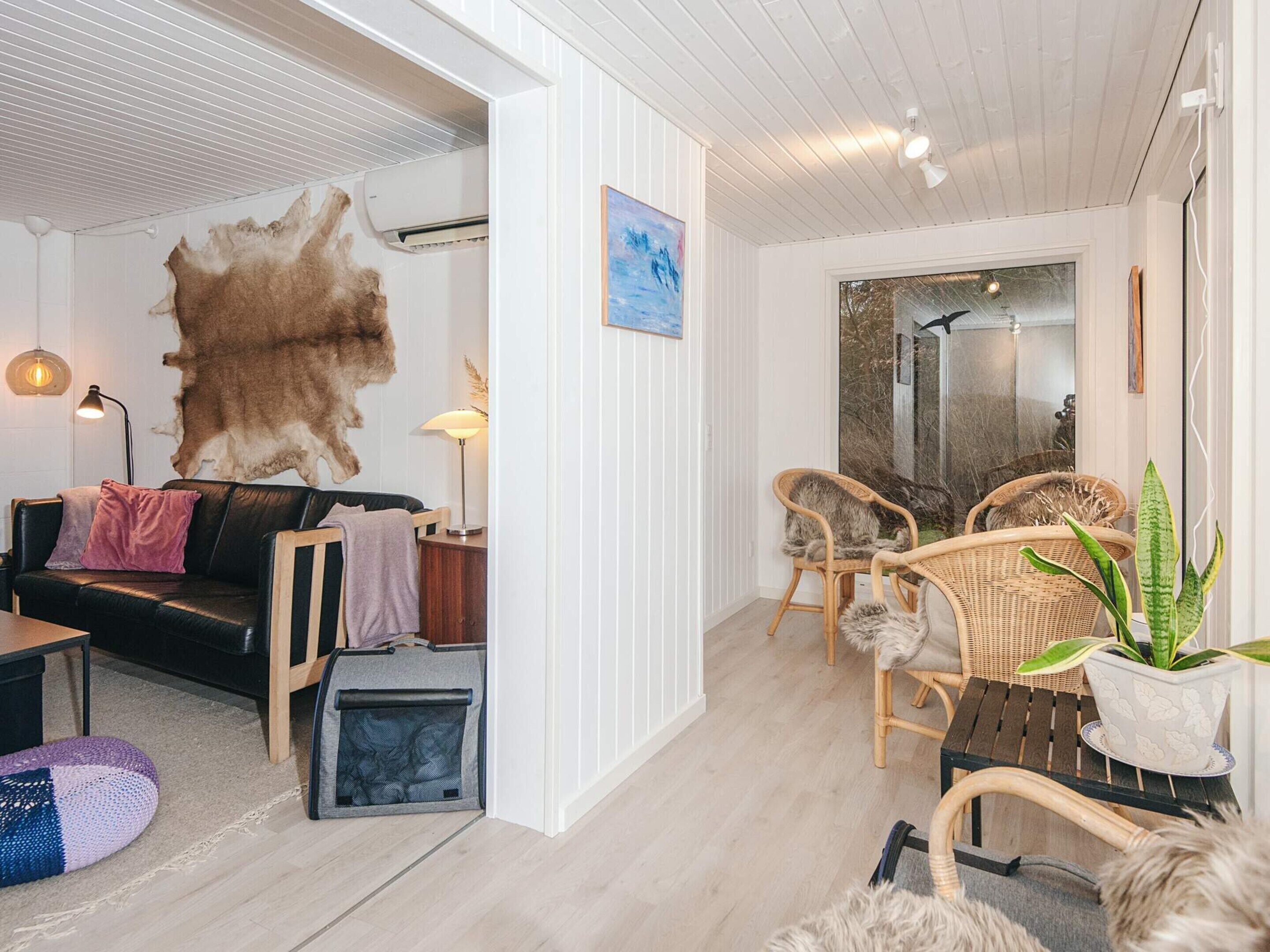 Ein modernes Wohnzimmer mit einem großen Fellteppich, einer schwarzen Ledersofa, Korbstühlen, einem kleinen Tisch und einem Blumentopf.