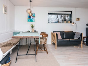 Un salon avec un banc en bois, une table à manger, un canapé en cuir noir et une fenêtre donnant sur des arbres.