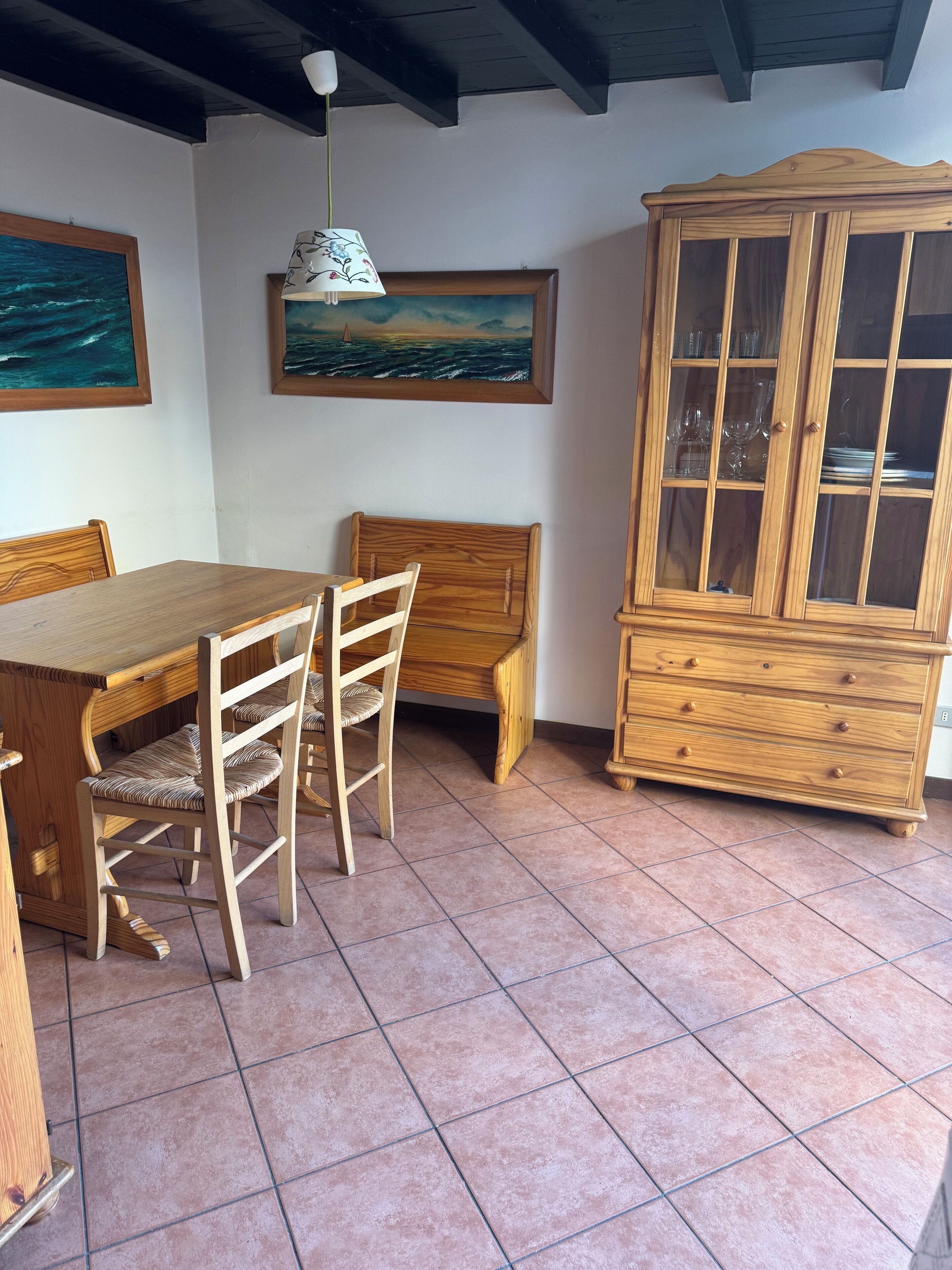 A dining area with a wooden table and chairs, a cabinet with glass doors, and two framed paintings on the wall.