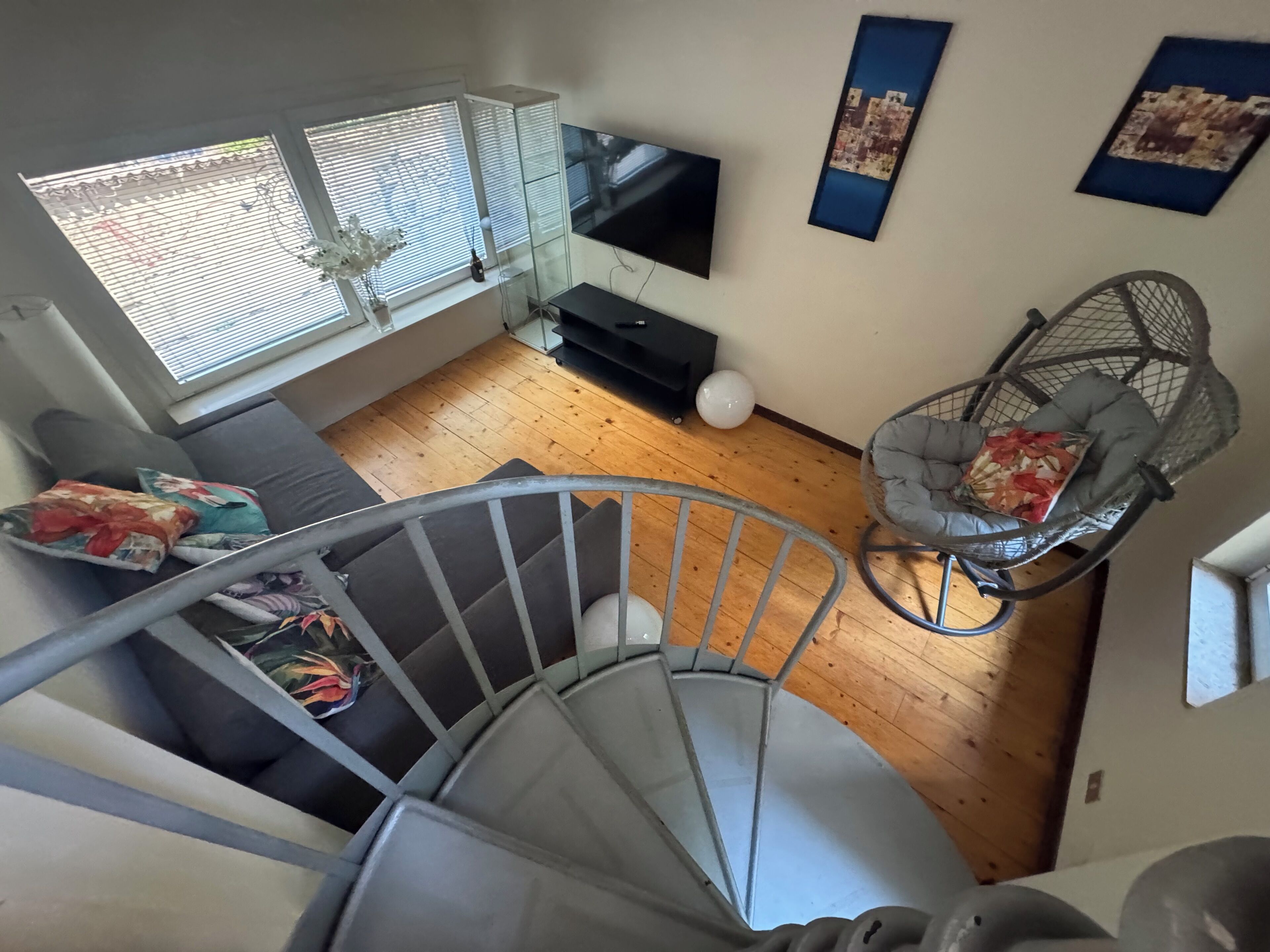 A modern living room with a staircase, a sofa, a TV, and a decorative chair.