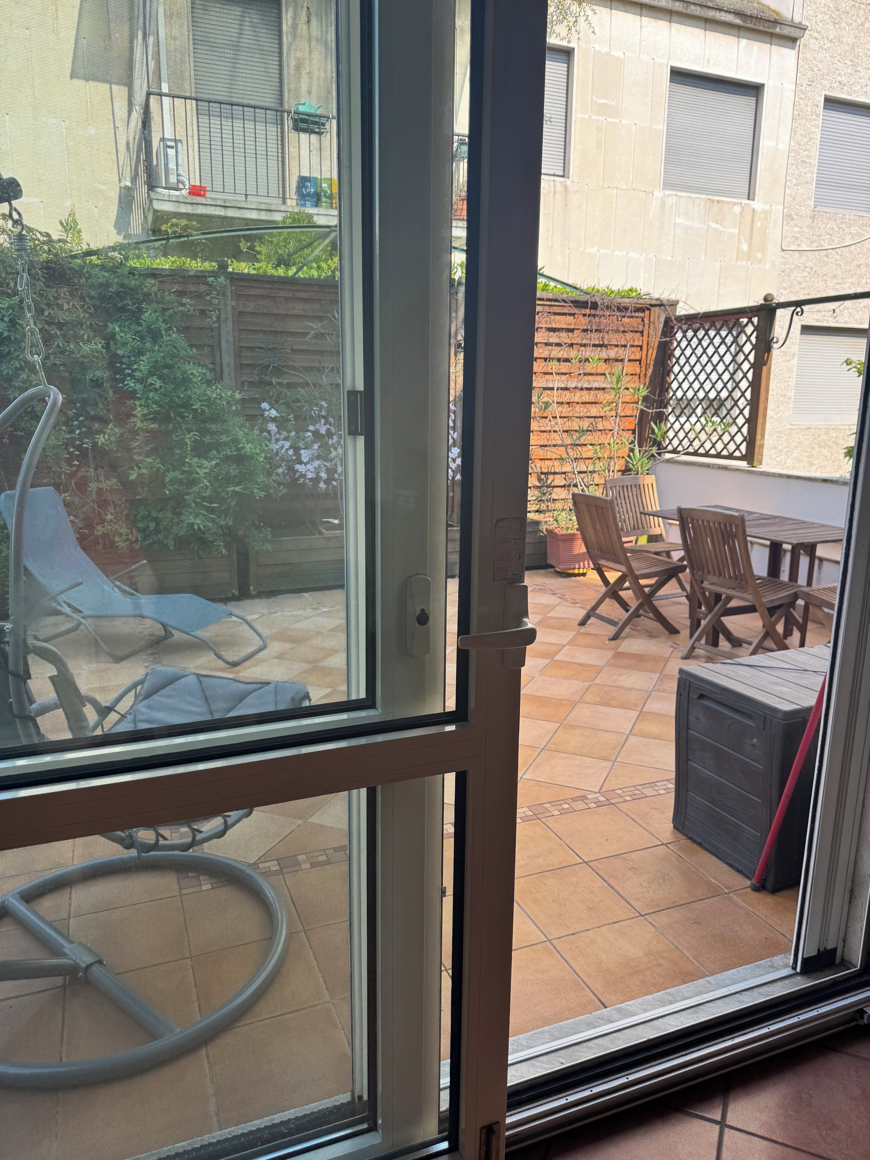 A patio area with a table and chairs, a swing, and a garden visible through a glass door.