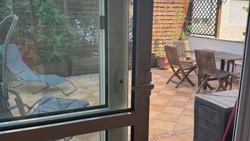 A patio area with a table and chairs, a swing, and a garden visible through a glass door.