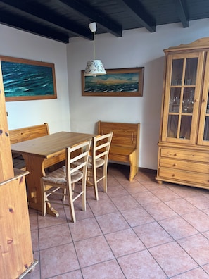 Zona pranzo con tavolo e sedie in legno, un mobile con ante in vetro e due quadri appesi al muro.