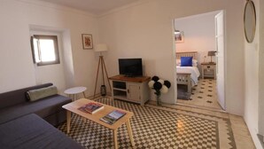 Ein Hotelzimmer mit Schachbrettmuster-Boden, einer Couch, einem Fernseher, einem kleinen Tisch mit Büchern, einer Lampe und einem Spiegel.
