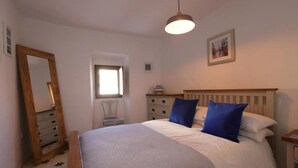 Ein Schlafzimmer mit einem großen Bett, einer Holzkommode, einem Stuhl, einem Fenster und einer Pendelleuchte.