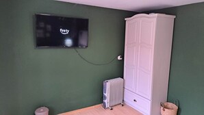 Una habitación con pared verde, un armario blanco, un radiador y un televisor que muestra el logotipo de Fire TV.
