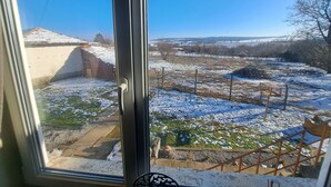 Vista a través de una ventana que muestra un paisaje nevado con cielo despejado, un jardín cercado y un edificio distante.