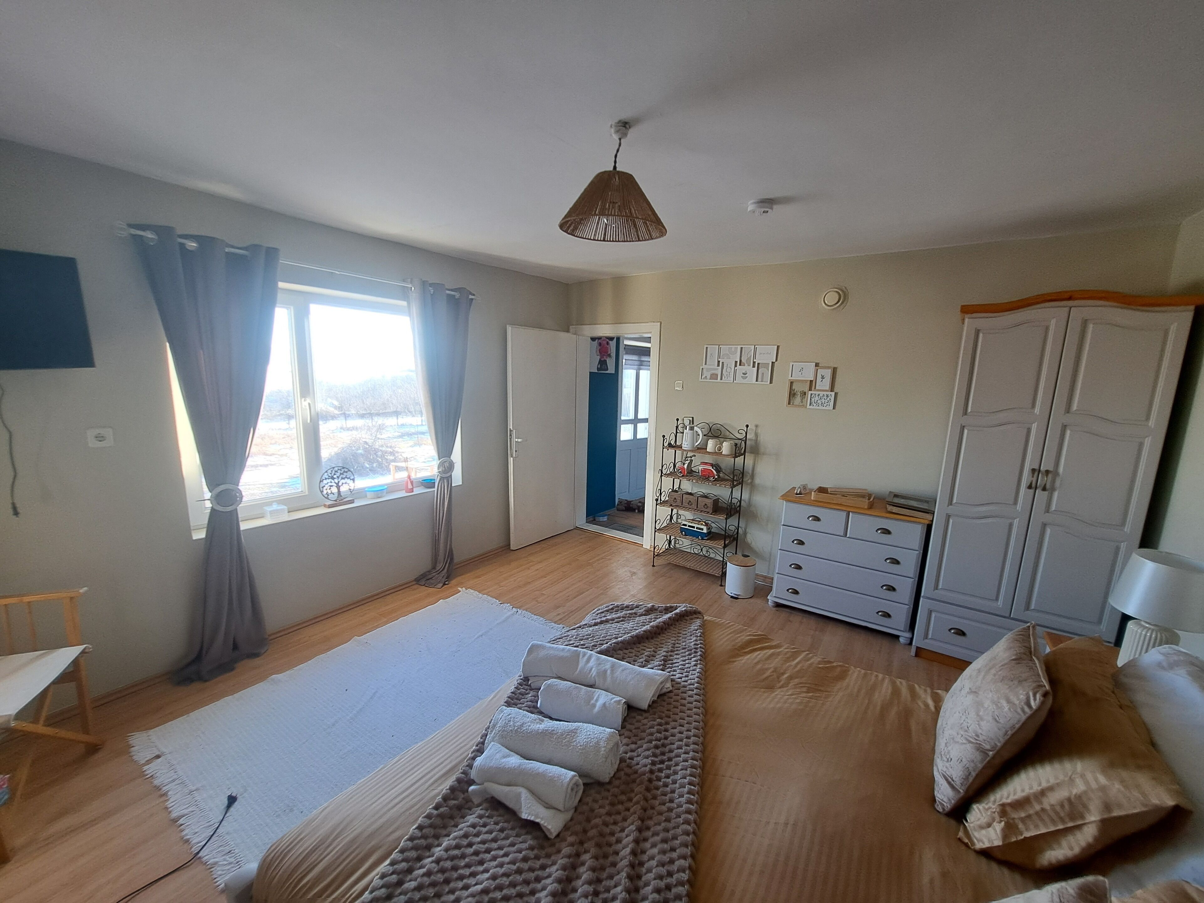 Un dormitorio amplio con una cama grande, un armario, un escritorio y un estante con diversos objetos.