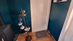 Una habitación con paredes verde azulado, una puerta blanca, un felpudo y una lámpara de metal decorativa, además de un cuadro con una vaca de caricatura.