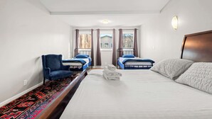 Ein Hotelzimmer mit einem großen Bett, zwei Einzelbetten, einem blauen Sessel und einem gemusterten Teppich.