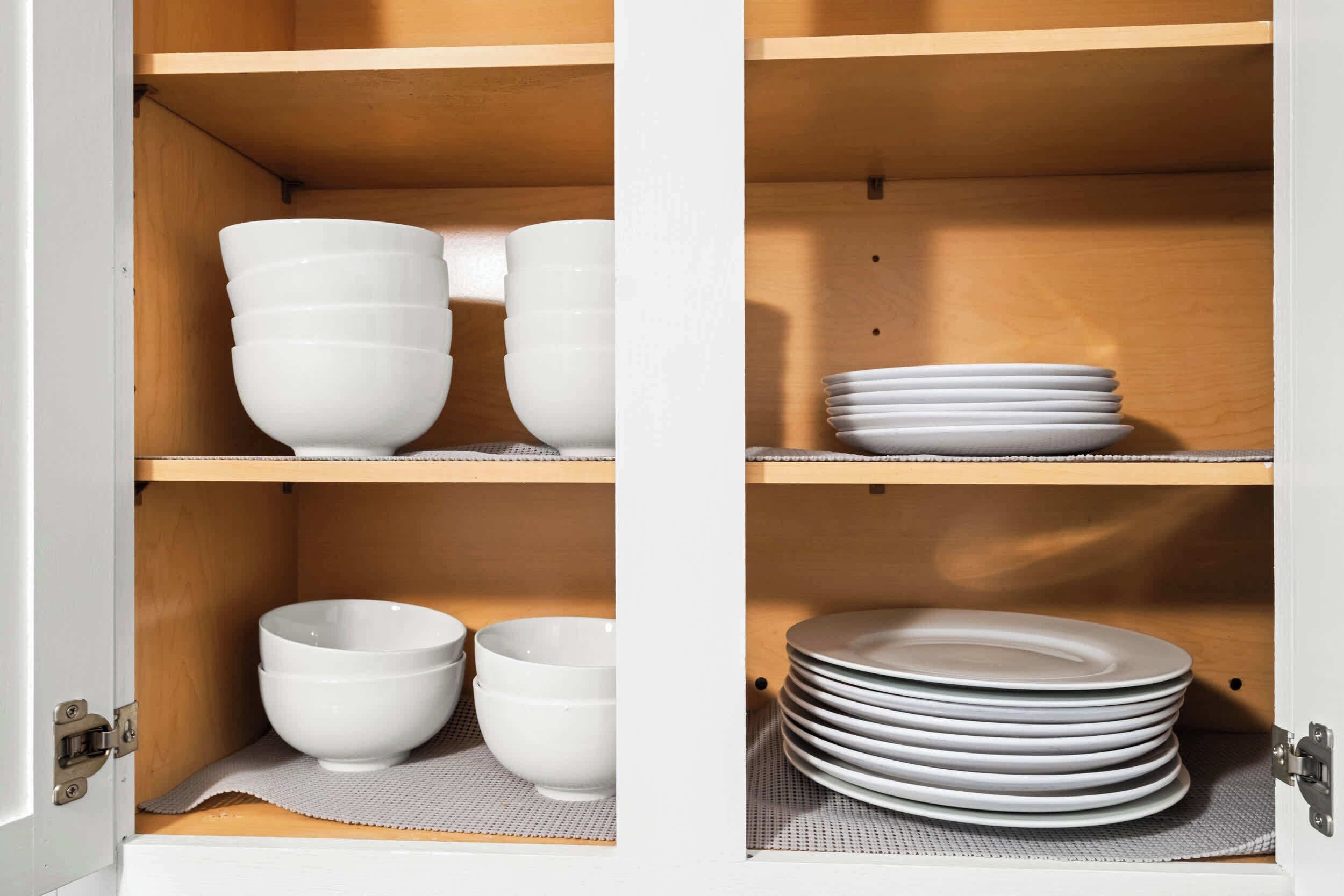 A kitchen cabinet with white bowls and plates.