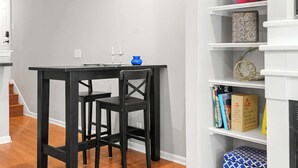 Ein Essbereich mit einem schwarzen Tisch und Stühlen, einer blauen Vase sowie einem Bücherregal mit Büchern und Dekoration.