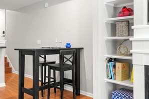 Ein Essbereich mit einem schwarzen Tisch und Stühlen, einer blauen Vase sowie einem Bücherregal mit Büchern und Dekoration.