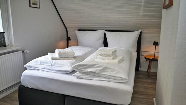A neatly made bed with white linens and towels, a black headboard, and a wooden floor. - The Lodge II - with private garden and beach chair (Büsum)