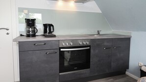 A modern kitchen with a built-in oven, a coffee maker, and a stainless steel countertop. - The Lodge II - with private garden and beach chair (Büsum)