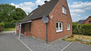 A brick house with a sloped roof, a satellite dish, and a small garden with a sign reading "The Lodge I". - The Lodge II - with private garden and beach chair (Büsum)