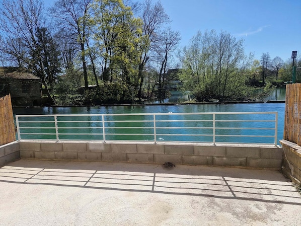 A concrete deck with a white railing overlooking a river, surrounded by trees and a stone wall. - **House by the Water – Dun-sur-Meuse – Wi-Fi – All Comforts** (Dun-sur-Meuse)