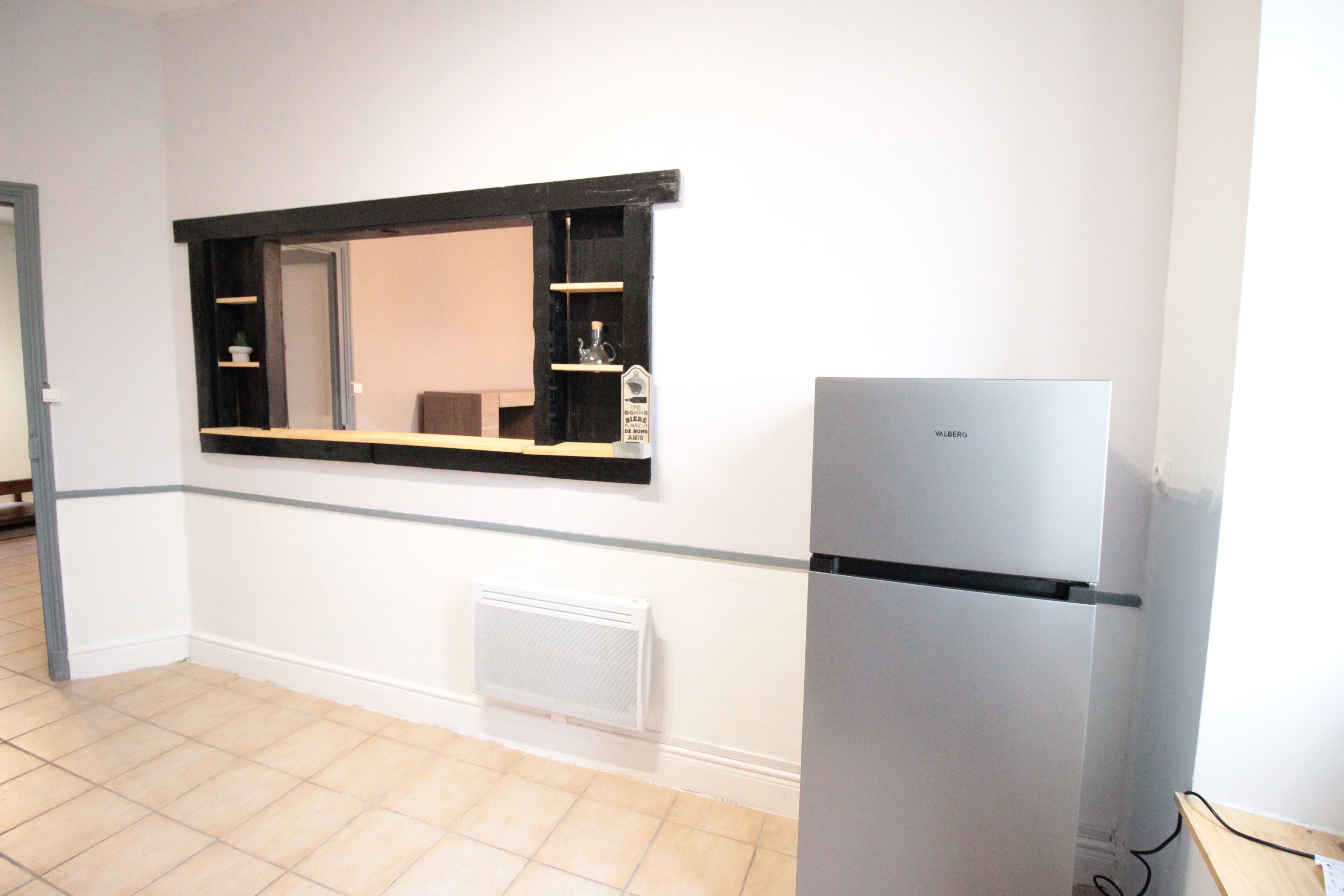 Una cocina con refrigerador empotrado, una ventana con repisas y un radiador blanco.