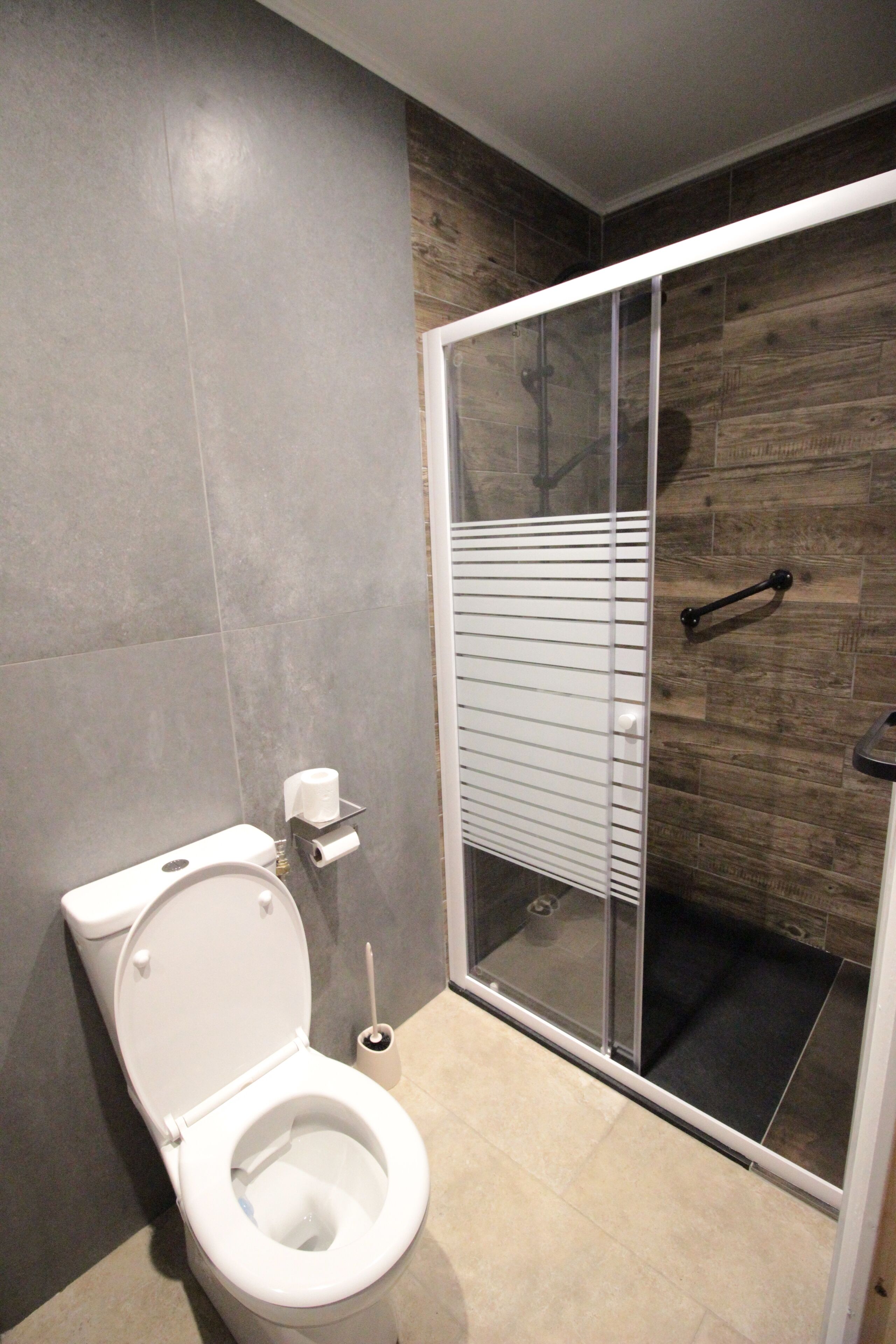 Une salle de bain moderne équipée de toilettes, d’une douche à parois de verre et d’un porte-rouleau de papier toilette.