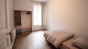 Un dormitorio con cama, armario empotrado, radiador y ventana con cortinas.